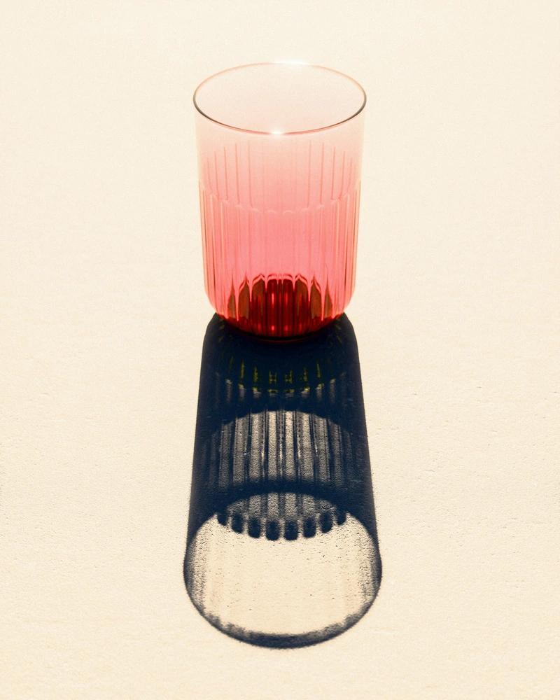 Een roze geribbeld glas werpt een lange, vervormde schaduw in het zonlicht.