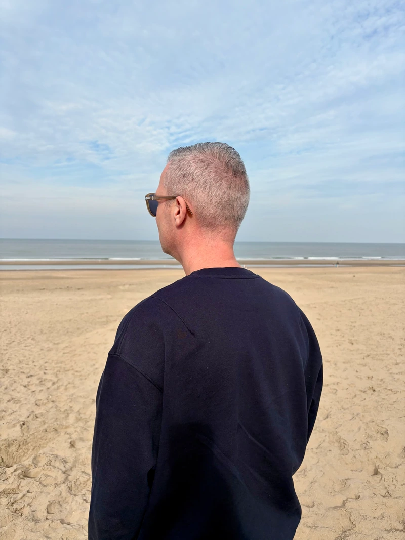 Een persoon van achteren en opzij gezien, uitkijkend over het strand en de zee.