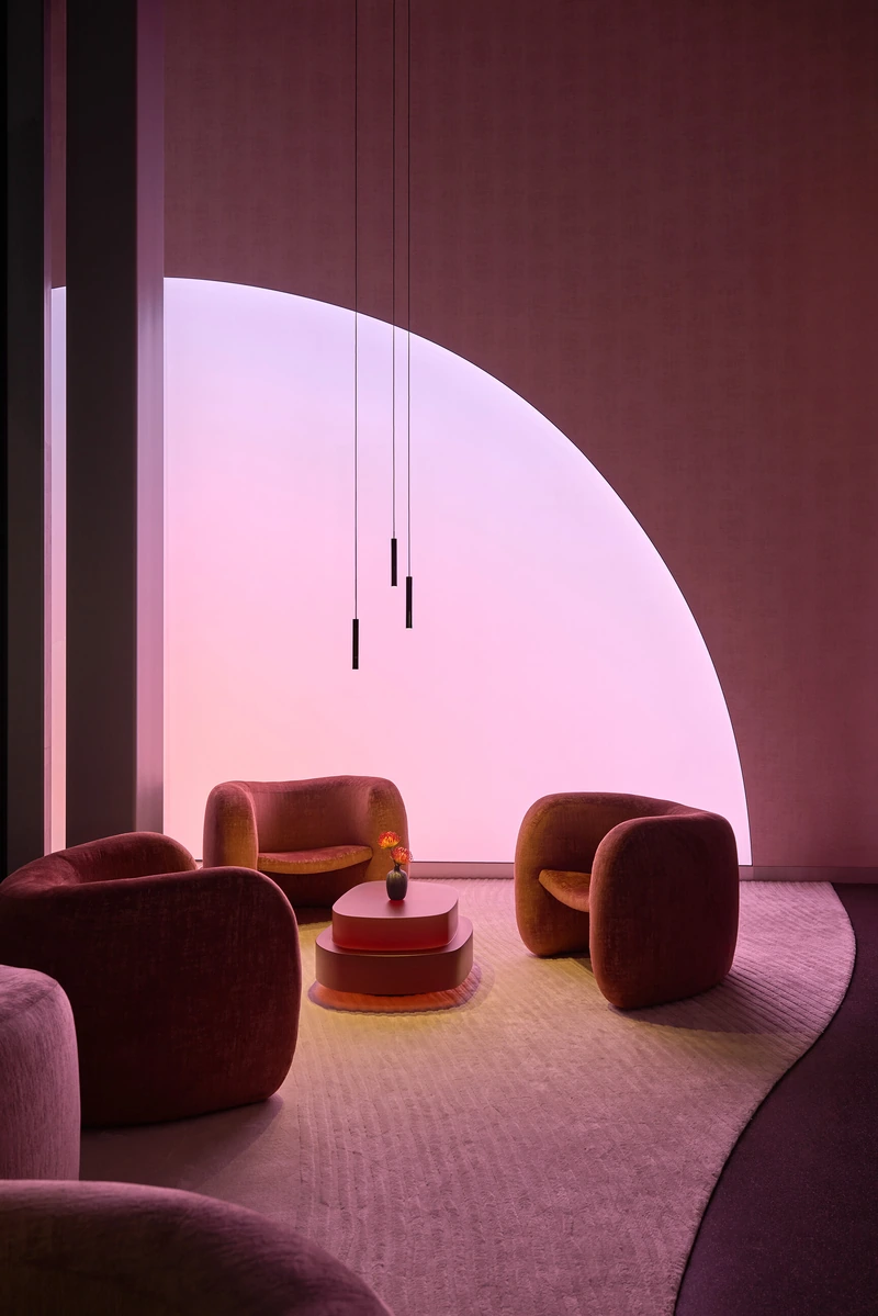 Een warme zithoek met fauteuils, een lage tafel en een grote roze lichtboog.